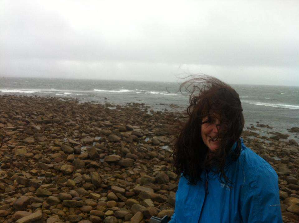Ann Marie Dunne on a rocky coastline in windy weather. Hair blowing in the wind.