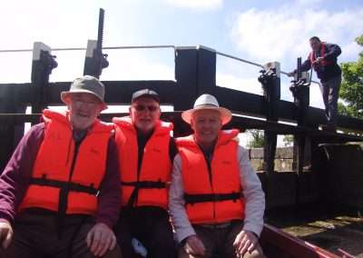 Three men wear orange lifejackets on a boat in a lock. Lock Keeper working the lock gates.