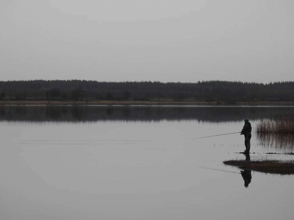 Fisherman on side of Lough O'Flynn lake in grey overcast day