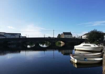 Small boats moored on river Barrow at Graiguecullen, Carlow, Ireland. Wellington bridge in background. Bright summers day