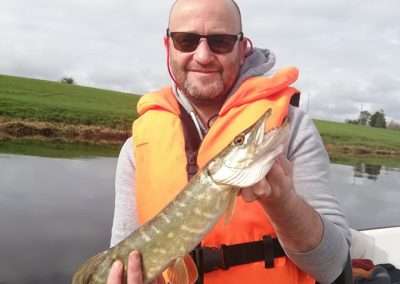 Mark Day holding a small Pike fish aboard a boat on river Barrow