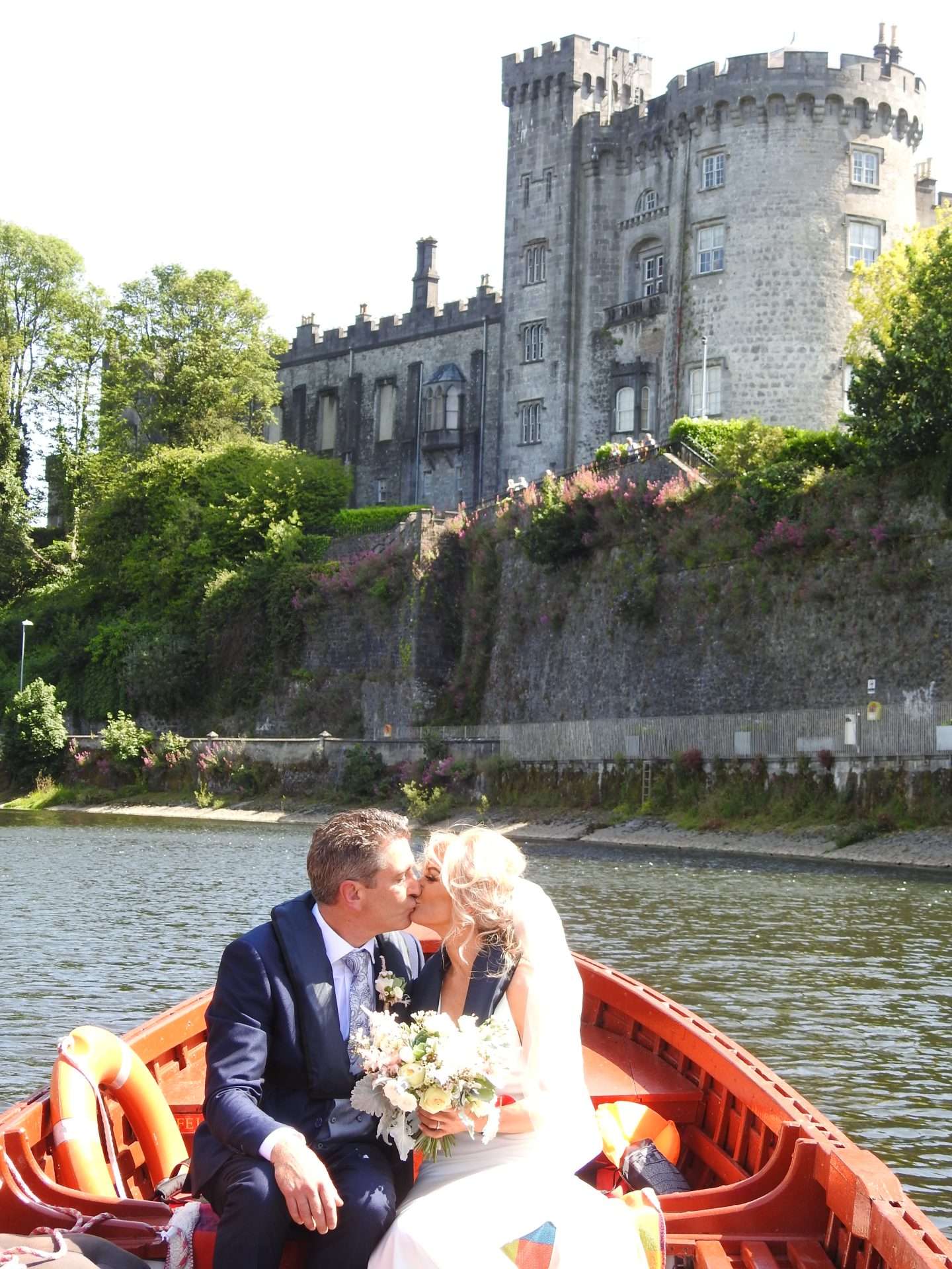 Wedding photo of newly married couple on a boat in Kilkenny city with Castle in background.